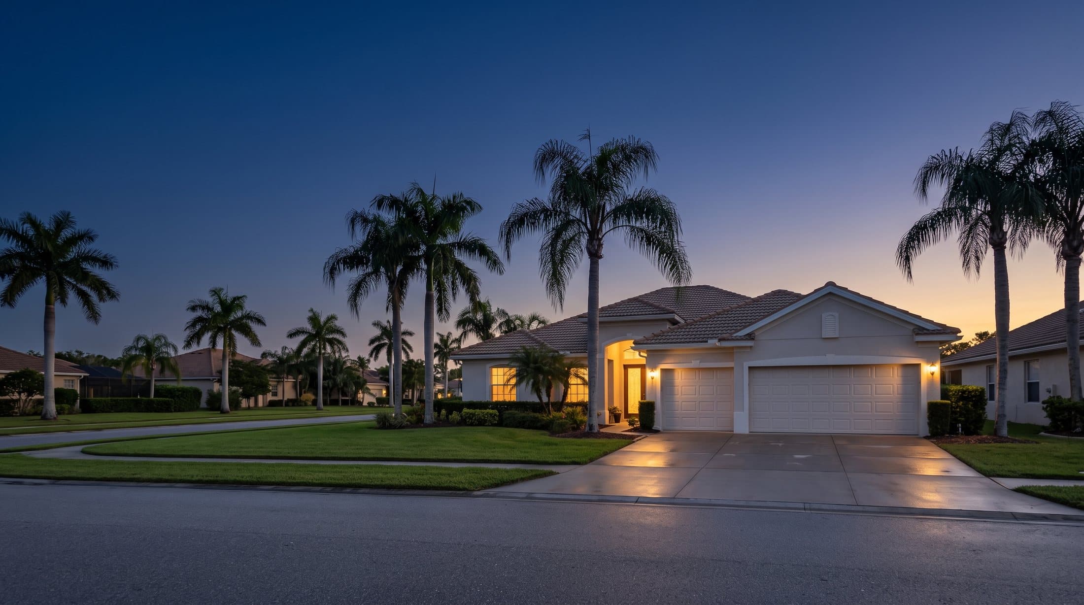 A Florida single-family home at blue hour with warm light in the windows, queen palms along the street and a three-car garage