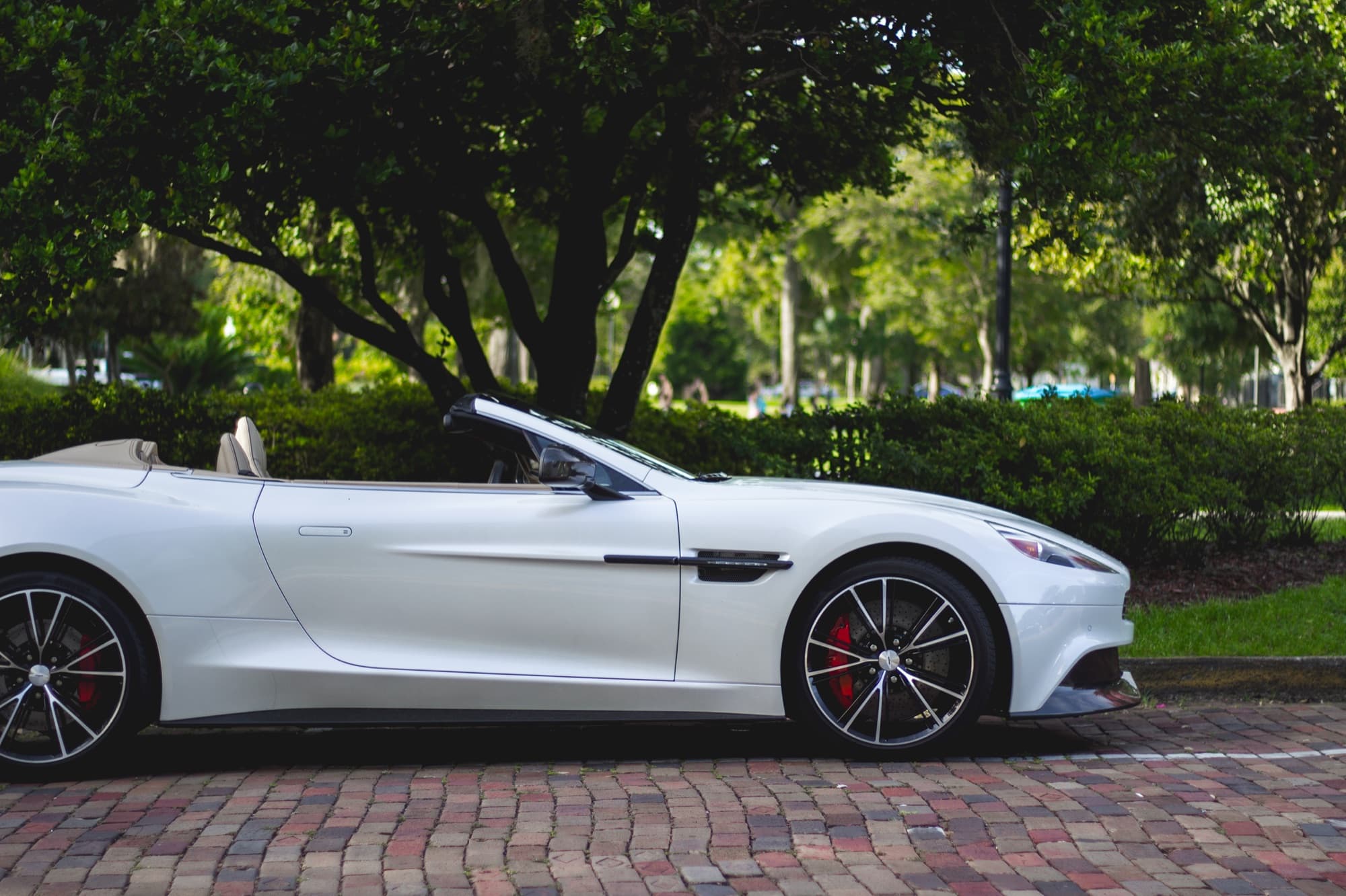 A white convertible sports car parked on a brick street under oak trees in Winter Park, Florida