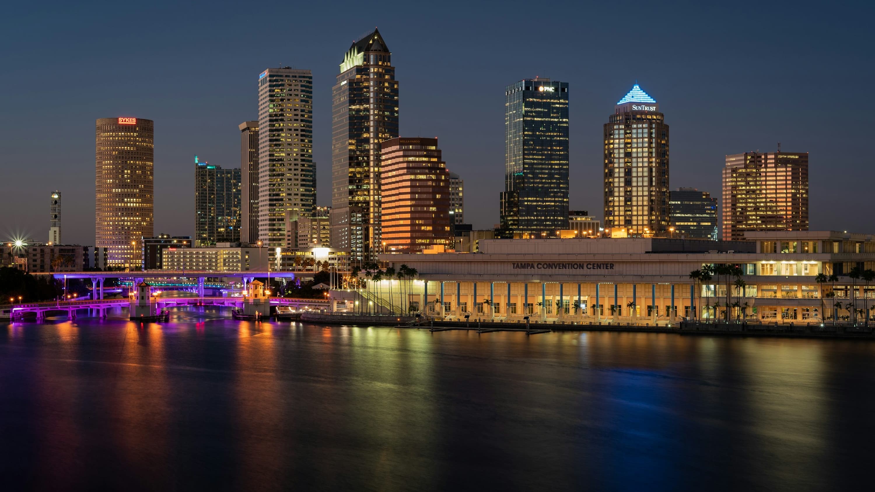 Ultra-wide night photograph of the Tampa downtown skyline with illuminated office towers reflecting on the water